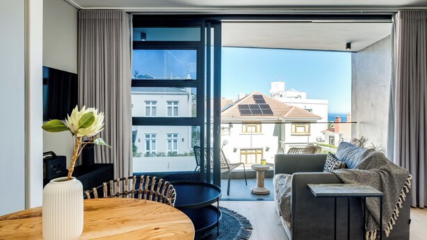 A modern living room with a dining area, large windows, and a view of buildings and the sea.