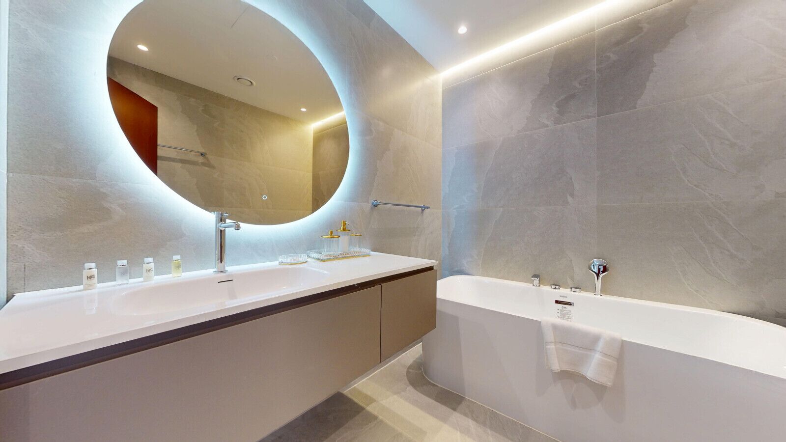 A modern bathroom with a large oval mirror, a double sink vanity, and a freestanding bathtub.