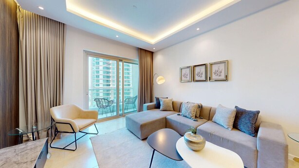 Een moderne woonkamer met een bank, fauteuils, een glazen salontafel en uitzicht op een wolkenkrabber door grote ramen.