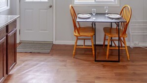 A dining area with a table set for two, wooden chairs, a window with blinds, and a door with a doormat. - Couple`s Romantic PEC Getaway (Prince Edward)