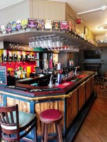A bar area with a wooden counter, stools, and a variety of bottles and glasses.