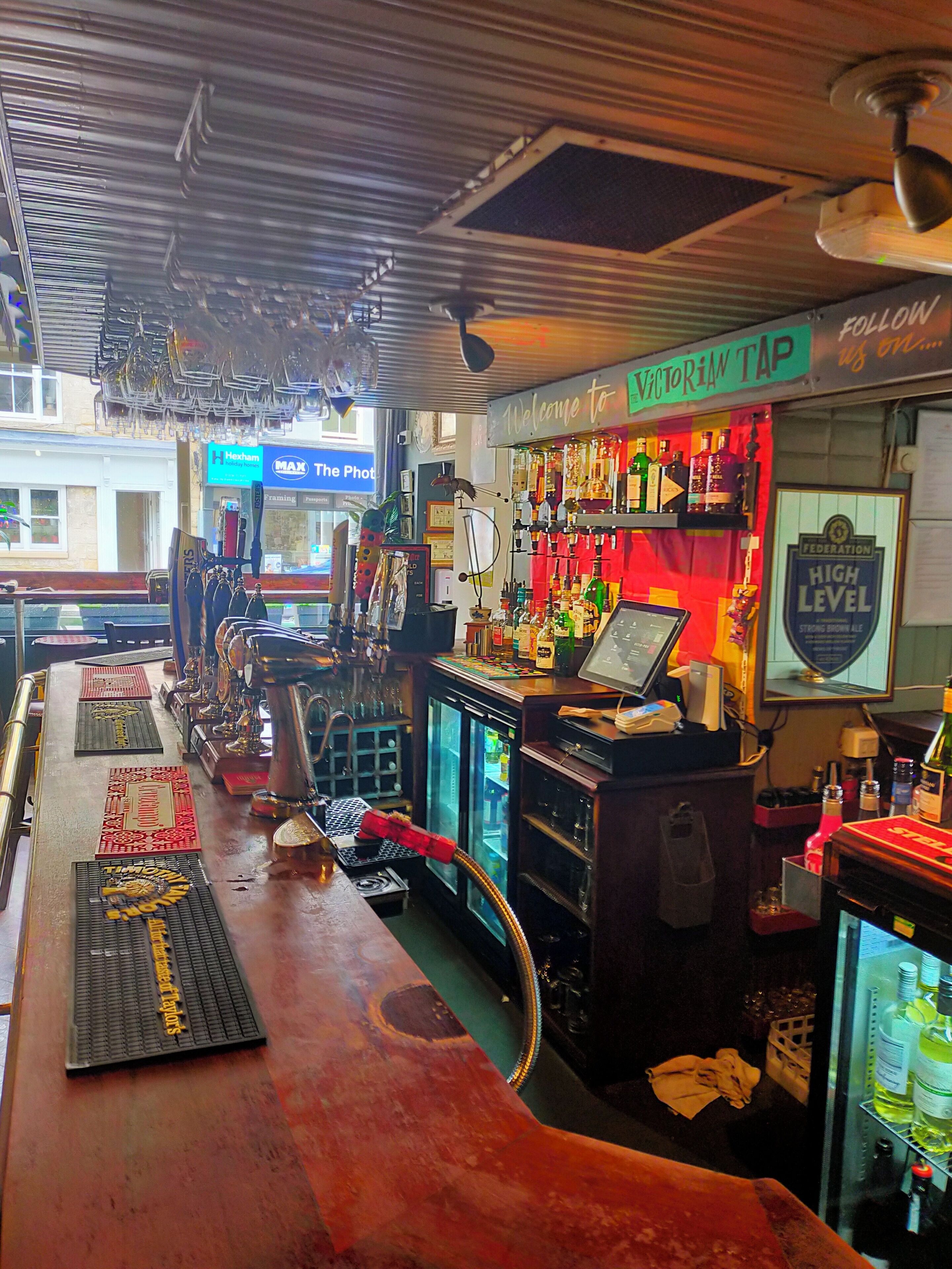 Een bar met een toonbank, barstoelen, een kassa en een koelkast.