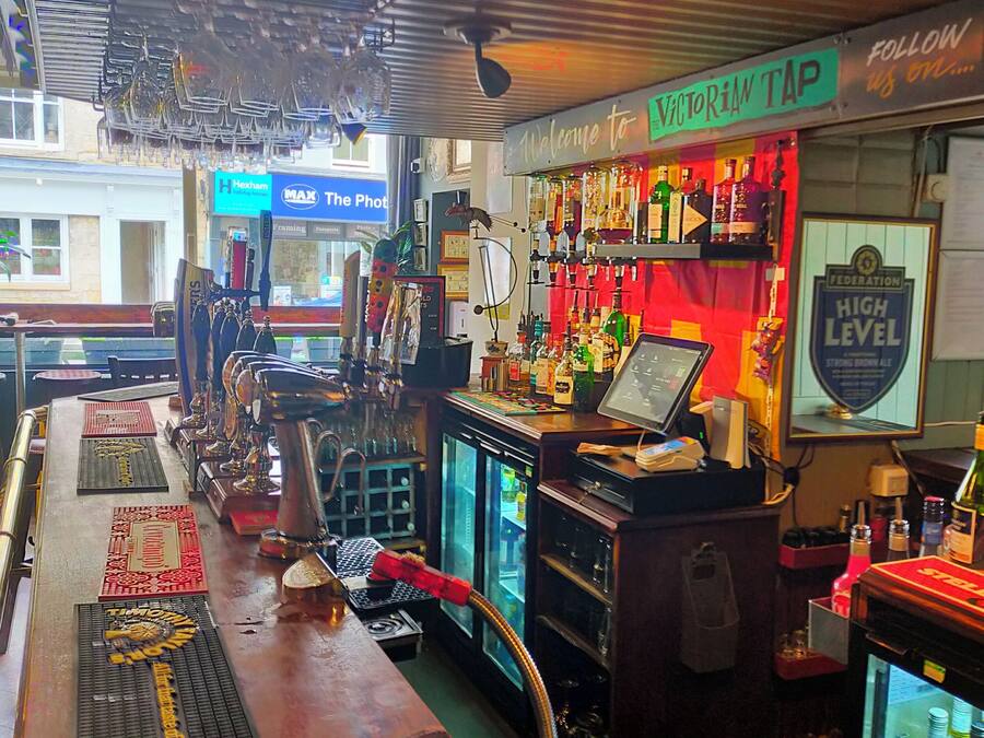 A bar area with a counter, bar stools, a cash register, and a refrigerator.