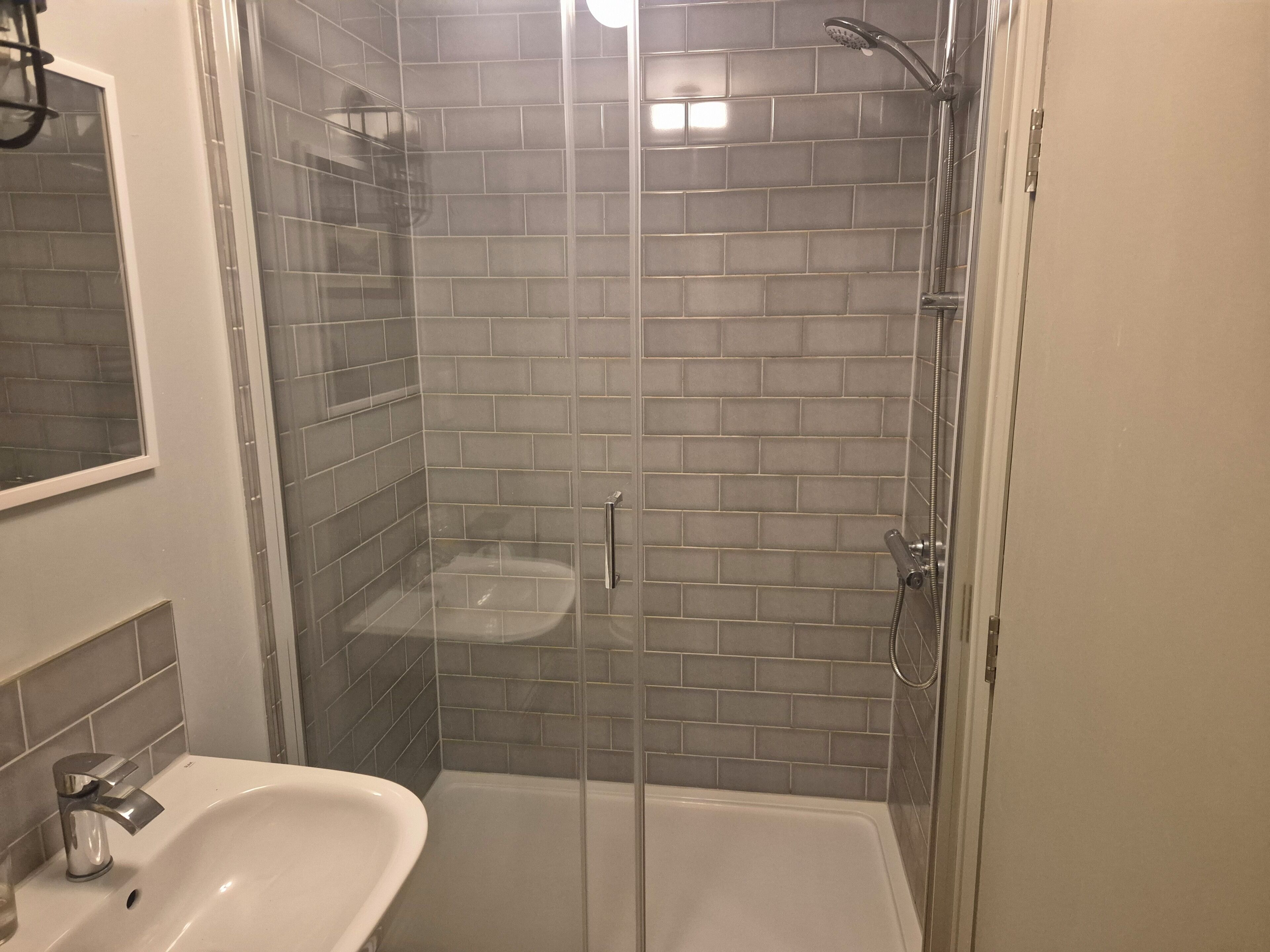 A bathroom with a glass-enclosed shower, a white sink, and tiled walls.