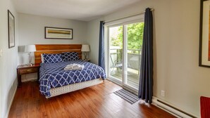 Ein Schlafzimmer mit Bett, Nachttischen, einem Fenster mit Vorhängen und einer Tür, die auf einen Balkon führt.