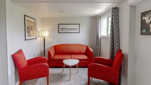 Ein Wohnzimmer mit einem roten Sofa, zwei roten Sesseln, einem weißen Couchtisch, einer Stehlampe und einem gerahmten Bild an der Wand.