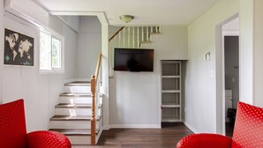 Eine Treppe mit einem hölzernen Geländer führt zu einer Zwischenebene, auf der ein Flachbildfernseher an der Wand befestigt ist.