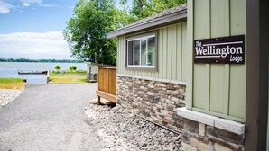 Una cabaña llamada "The Wellington Lodge" con fachada de piedra y madera, un camino de grava que lleva a un muelle, y vista al lago.