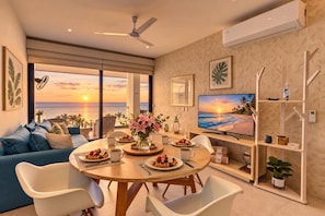 A modern living room with a large TV, dining table with breakfast, and a view of the ocean. - Golden Hour & Ocean Views (Nuevo Vallarta)
