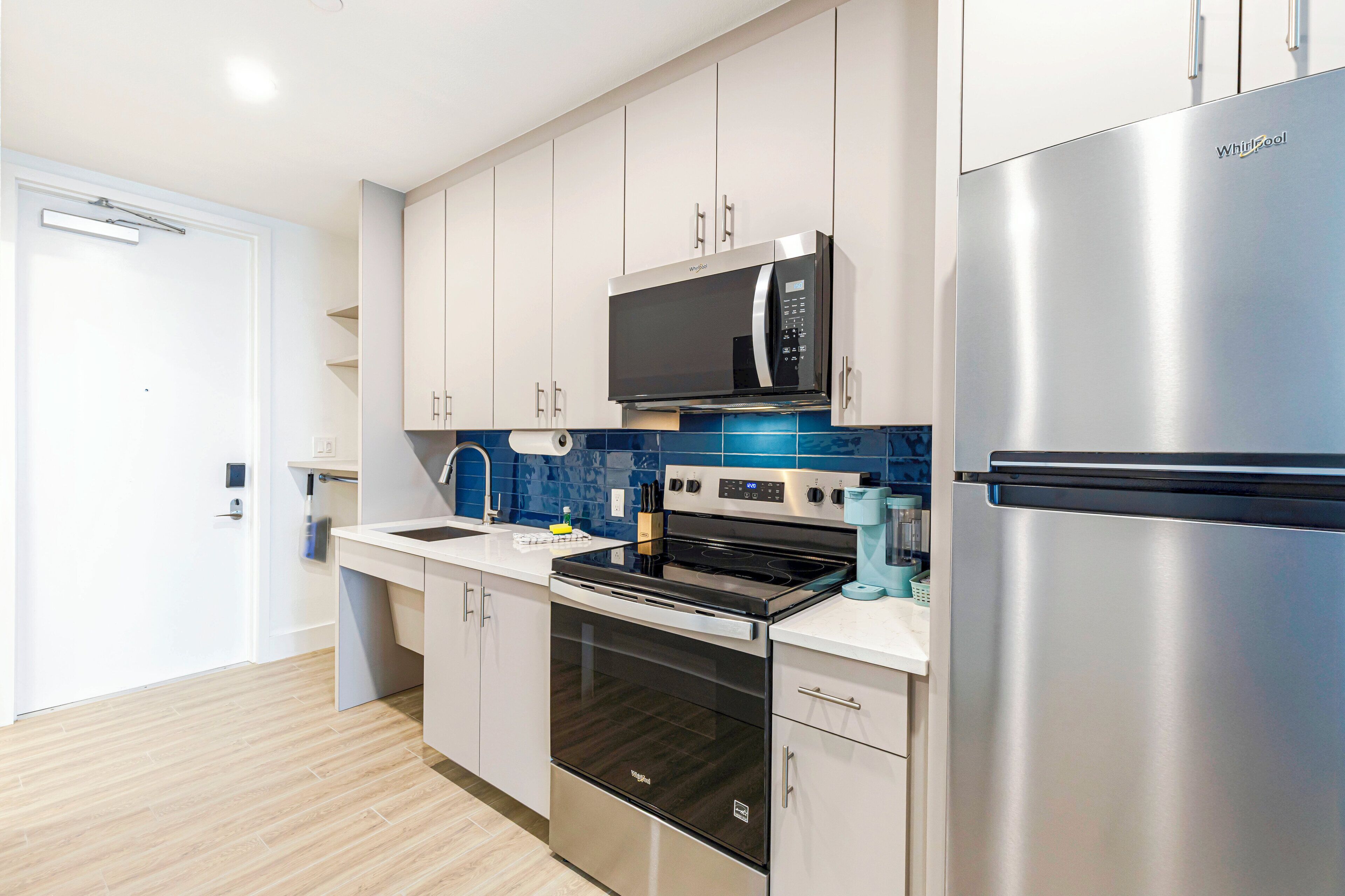 A modern kitchen with stainless steel appliances, white cabinets, and a blue backsplash.