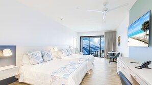 A hotel room with a large bed, a desk, a chair, and a view of the beach through the window. - Shalimar Beach Resort (Sanibel)