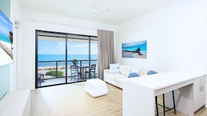 A modern room with a large sliding glass door leading to a balcony with a view of the beach. There is a white sofa, a small table, and a white desk with a chair. - Shalimar Beach Resort (Sanibel)
