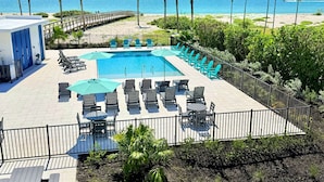A pool area with lounge chairs and umbrellas, a wooden deck, and a view of the beach and ocean. - Shalimar Beach Resort (Sanibel)