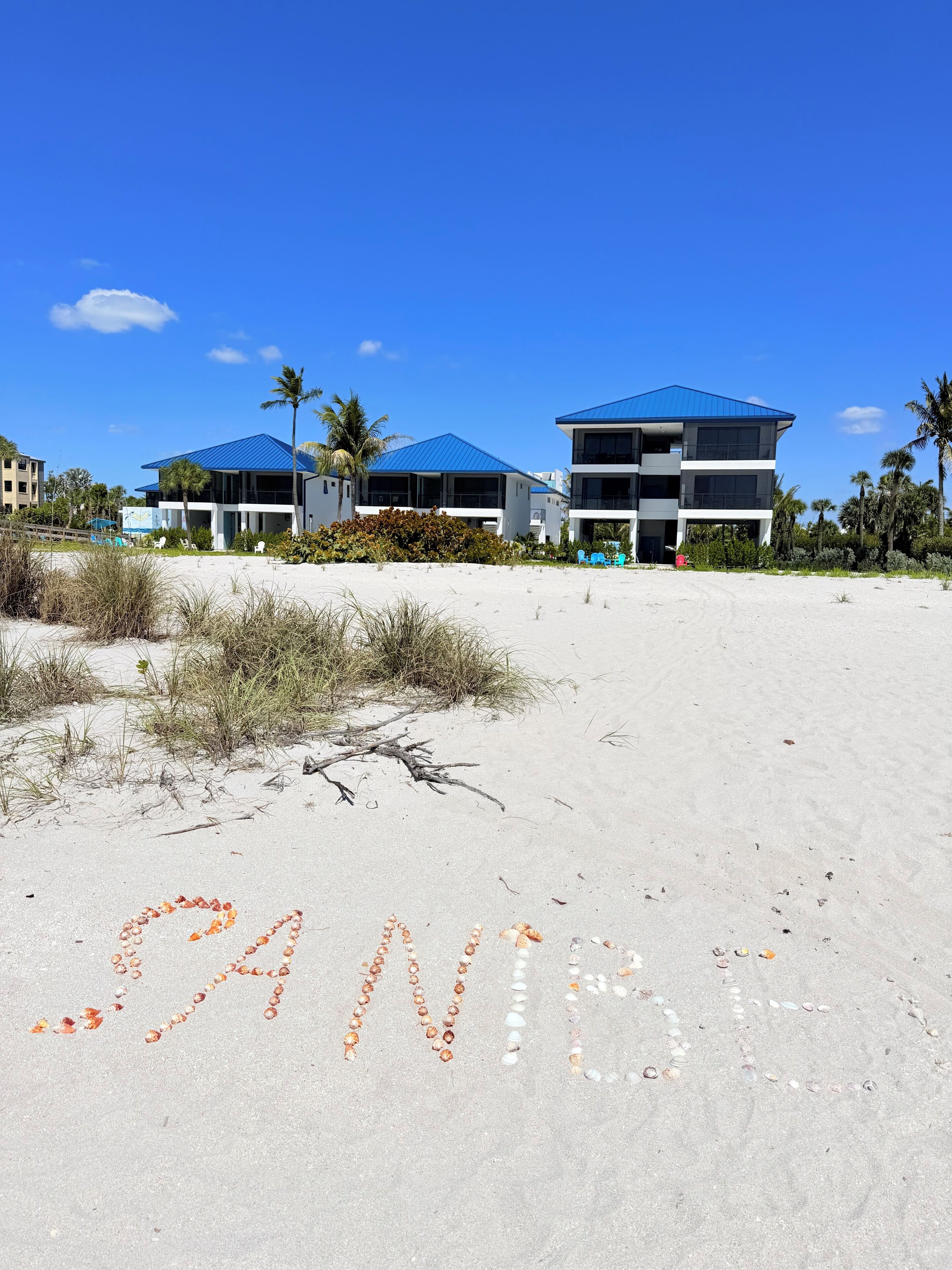 A beachside hotel with a sandy foreground and a clear blue sky.