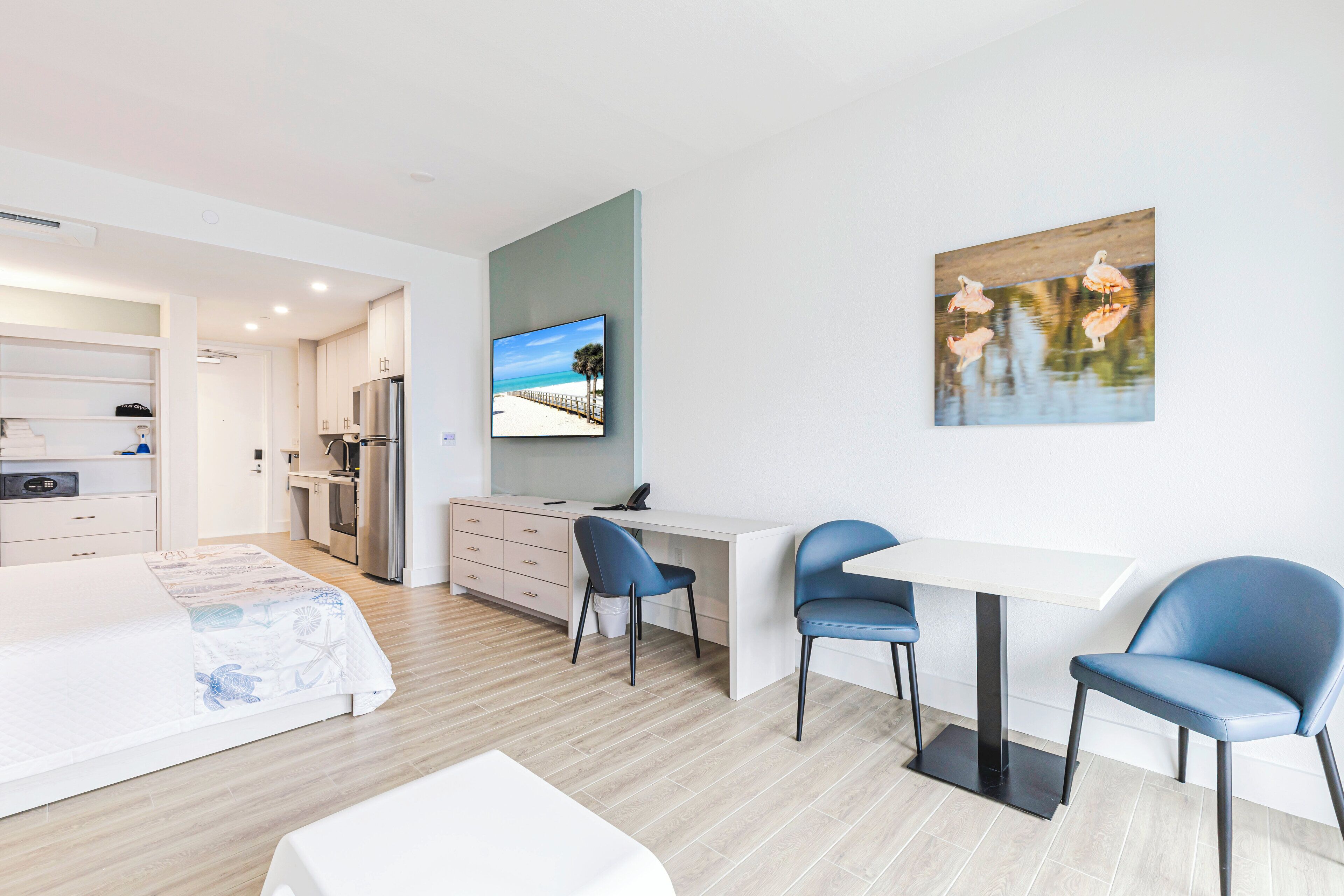 Une chambre d’hôtel moderne équipée d’un lit, d’un bureau, de deux chaises, d’une télévision et d’un tableau.