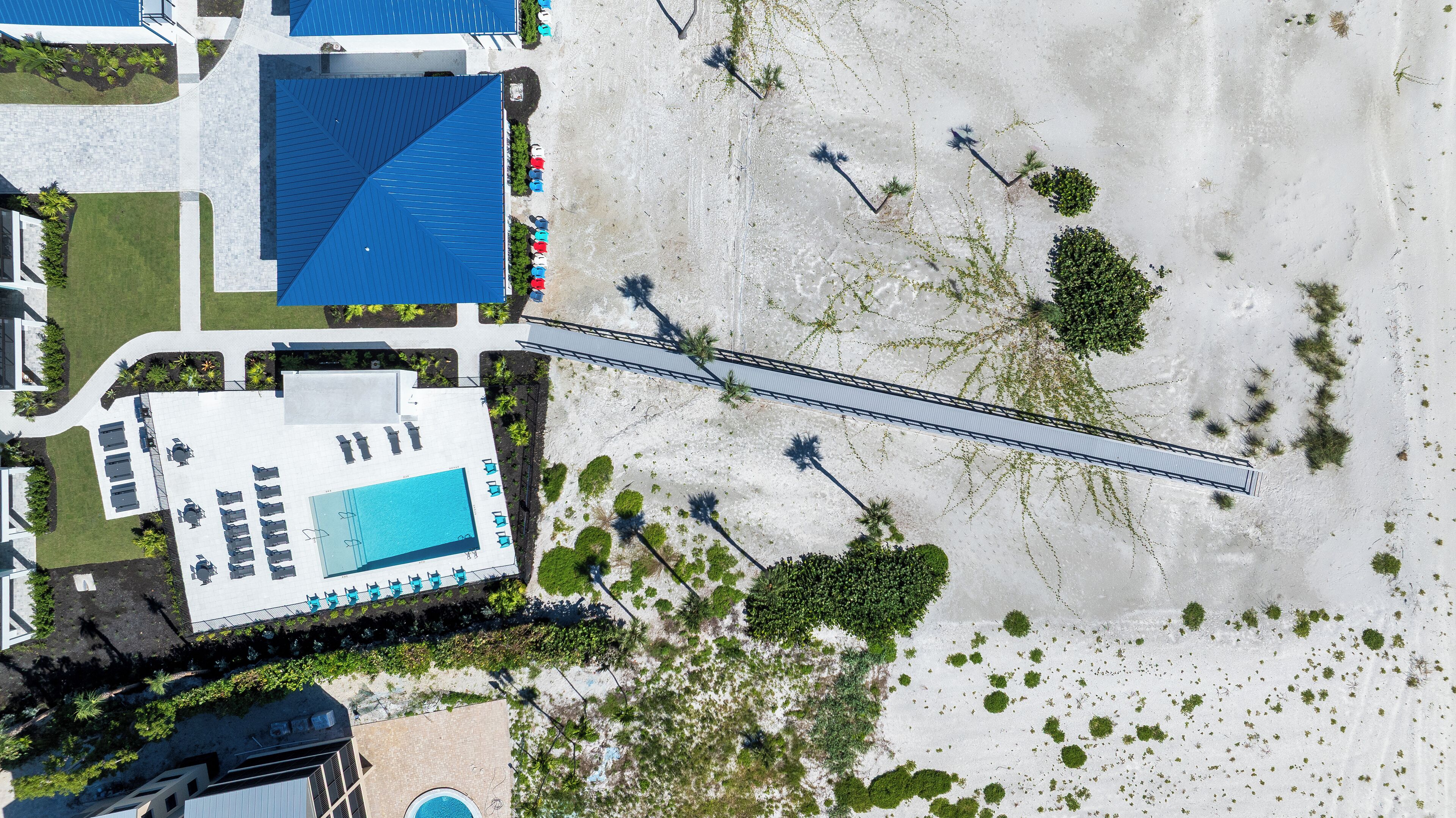 An aerial view of a resort with a swimming pool, a bridge, and a beach area.