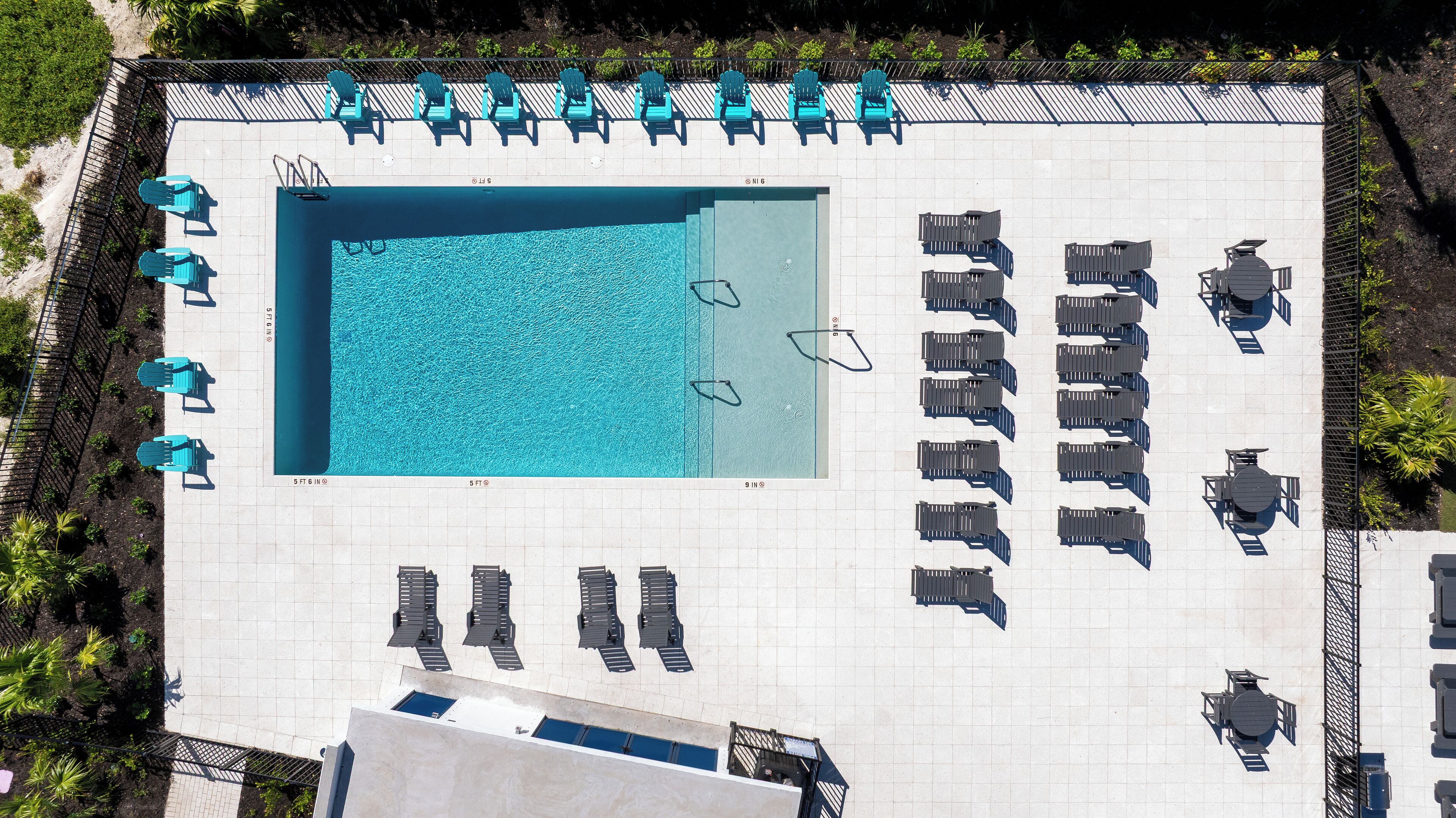 An aerial view of a pool area with multiple lounge chairs and tables arranged around a central swimming pool.