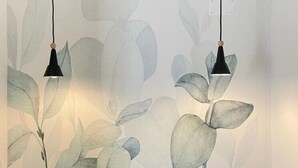 A bedroom with a bed, two pendant lights, and a wall with a leaf pattern.