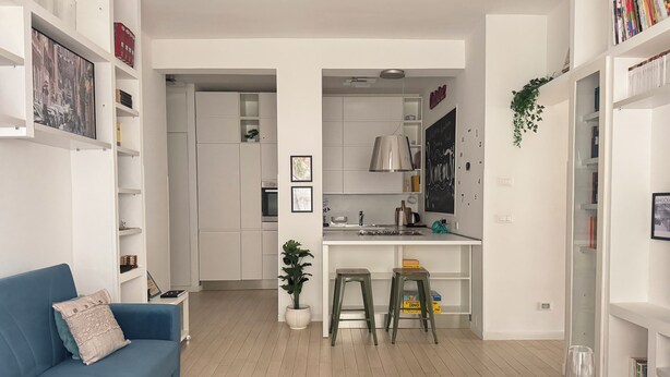 Un appartement moderne avec un canapé bleu, une table à manger avec des verres, une cuisine avec des meubles blancs et une bibliothèque.