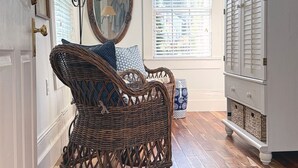A room with a wicker chair, a mirror, a cabinet, and a window with blinds.