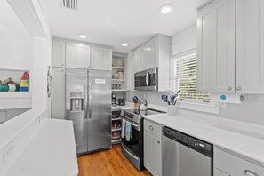 A modern kitchen with white cabinetry, stainless steel appliances, and a wooden floor.