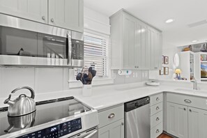Una cocina moderna con electrodomésticos de acero inoxidable, armarios blancos y un hervidor en la hornilla.