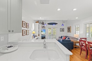 A modern kitchen with a central island, a dining area with a red chair, and a living room with a blue sofa. - Seabatical! 3BR 2BA Coastal Retreat for 8 Relax, Unwind, and Recharge (Panama City Beach)