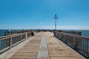 Eine hölzerne Pier, die sich ins Meer erstreckt, mit Menschen, die dort angeln und spazieren gehen.