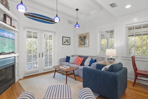 A living room with a sofa, coffee table, striped ottoman, and a television. - Seabatical! 3BR 2BA Coastal Retreat for 8 Relax, Unwind, and Recharge (Panama City Beach)