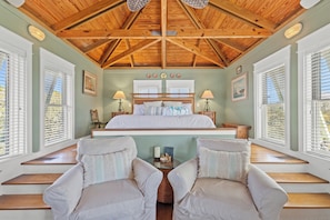 A bedroom with a wooden ceiling, a large bed, two bedside tables with lamps, and a view through the window. - Seabatical! 3BR 2BA Coastal Retreat for 8 Relax, Unwind, and Recharge (Panama City Beach)