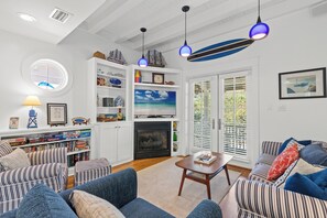 A living room with a fireplace, bookshelves, a television, and a striped sofa. - Seabatical! 3BR 2BA Coastal Retreat for 8 Relax, Unwind, and Recharge (Panama City Beach)