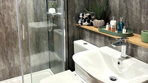 Un baño moderno con cabina de ducha de vidrio, inodoro blanco y lavamanos con estante de madera arriba.