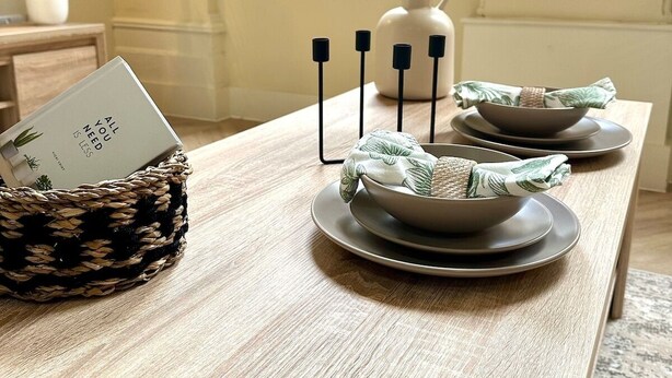 Una mesa de comedor con una cesta tejida, un florero con plumas de pampa y un candelabro.