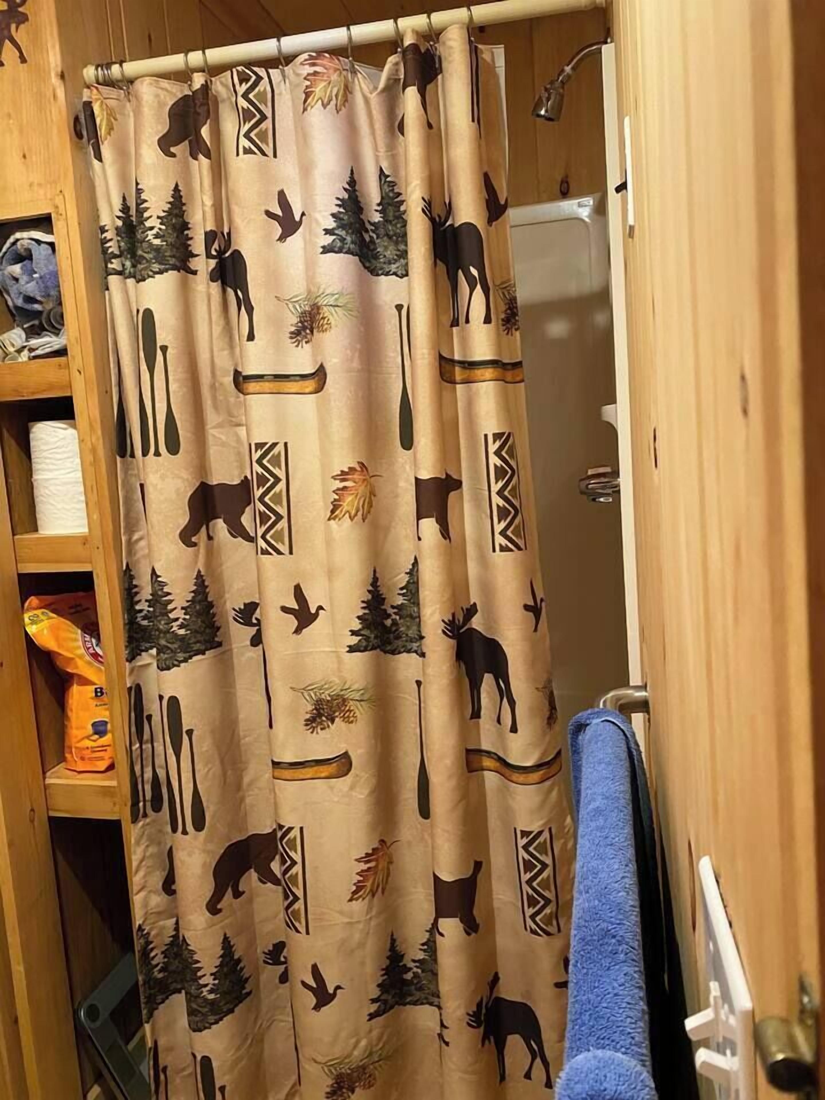 A bathroom with a shower curtain featuring wildlife prints, a wooden shelf with towels, and a blue towel hanging on the wall.