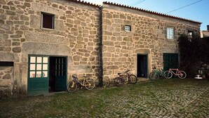 A stone building with two green doors and windows, a cobblestone courtyard, and bicycles parked outside. - 2Br Serra da Estrela Escape-cheese & Wine, Parking (Celorico da Beira)