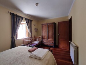 Ein Schlafzimmer mit Bett, Holzschrank, Heizkörper und einem Fenster mit Vorhängen.