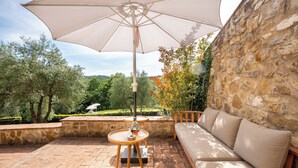 Eine Terrasse im Freien mit einer Steinsäule, einem beigen Sofa und einem Tisch mit Sonnenschirm.