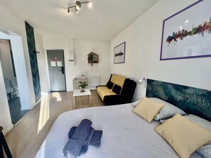 A modern hotel room with a large bed, a small table, a sofa, and a view of the city skyline.