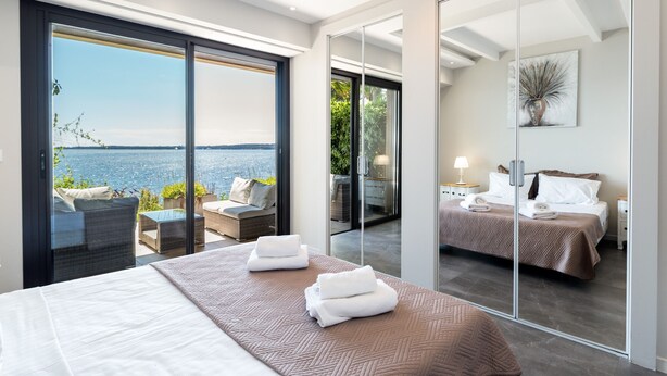 Een moderne hotelkamer met een groot bed, een balkon met uitzicht op zee en een apart slaapkamer met een grote spiegel.