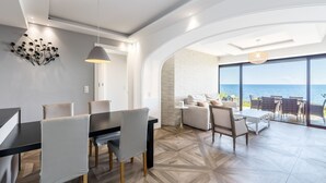 Een moderne eetruimte met een zwarte tafel en grijze stoelen, een witte wanddecoratie en uitzicht op de oceaan door grote ramen.