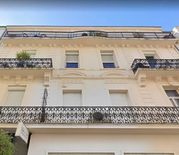 Un edificio con fachada blanca, balcones de hierro decorativo y un cielo azul despejado.