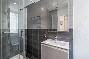 Uma casa de banho moderna com chuveiro em cabine de vidro, lavatório branco e espelho em cima.