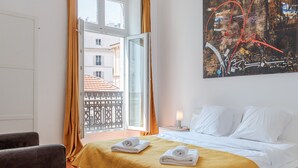 A hotel room with a bed, two towels, a nightstand, a lamp, and a painting on the wall. - - (Cannes)