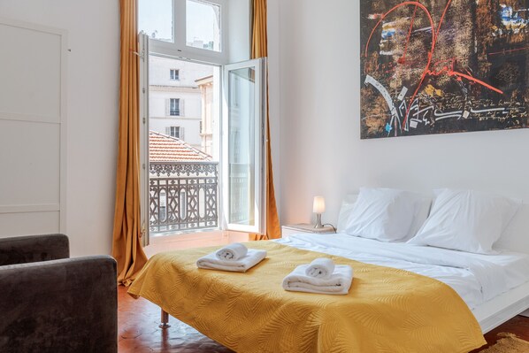 Quarto de hotel com uma cama, duas toalhas, uma mesinha de cabeceira, um abajur e um quadro na parede.