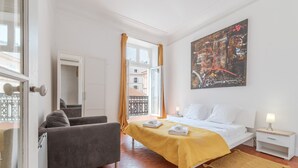 A hotel room with a bed, a sofa, a nightstand, a painting, and a view through a window. - - (Cannes)