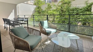 Un balc ón con mobiliario de mimbre, una mesa de vidrio y vistas a edificios y follaje.