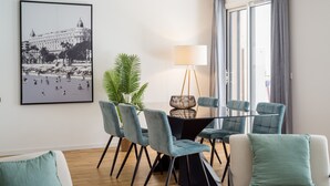 A dining area with a table and chairs, a potted plant, and a framed photograph on the wall.