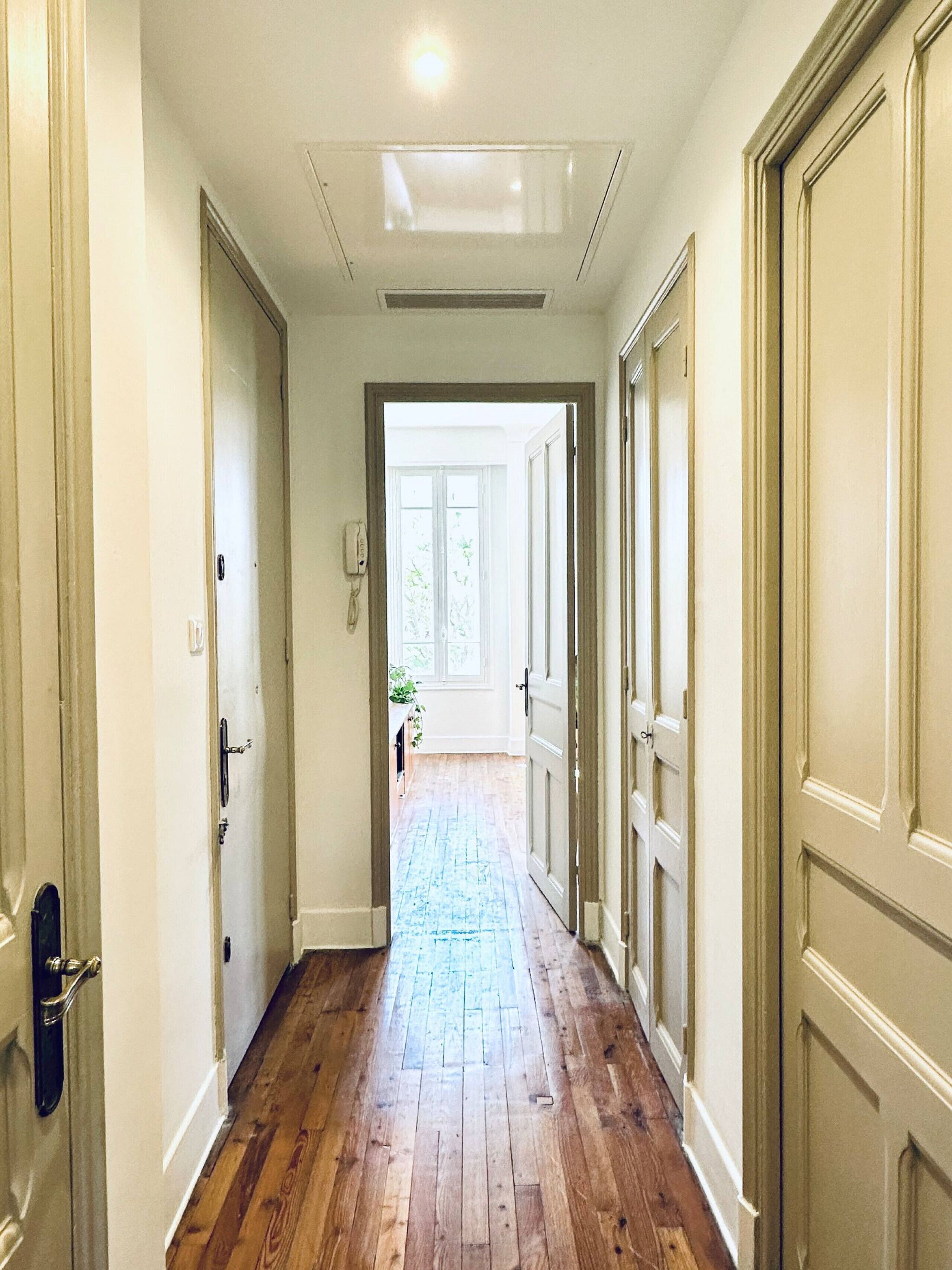 A hallway with wooden flooring, white walls, and doors leading to other rooms.