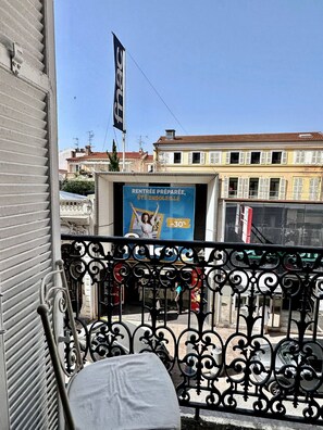 Un balcone con ringhiera in ferro battuto, una sedia bianca e un edificio con un cartello blu che pubblicizza un'offerta.