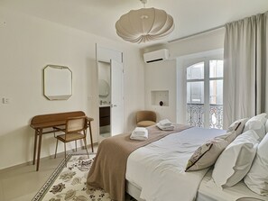 A hotel room with a bed, a desk, a chair, a window with curtains, and a decorative ceiling light.
